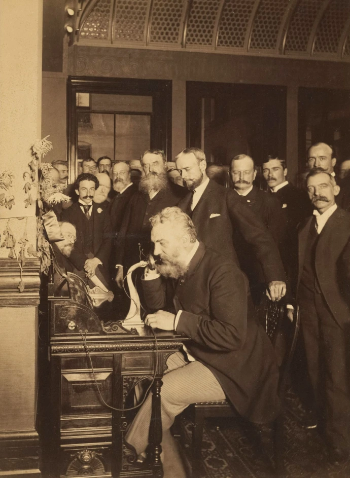 Men gathered around alexander graham bell using the telephone